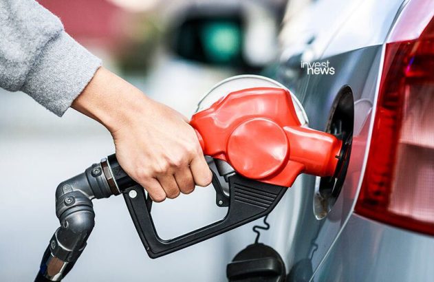 Mão bombeando gasolina em carro cinza com bico vermelho.