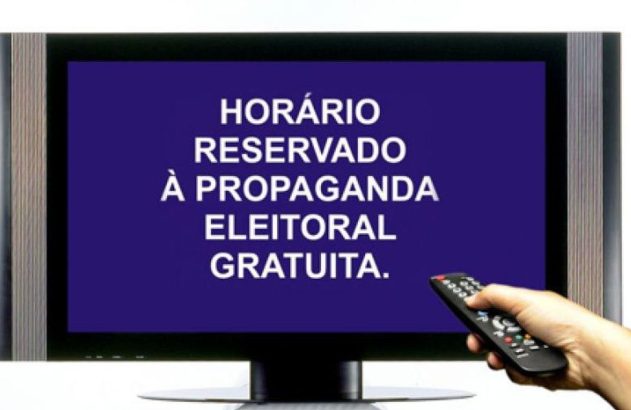 TV exibe mensagem de horário eleitoral gratuito, com mão segurando controle remoto.