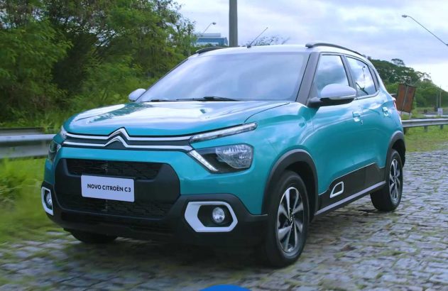 Novo Citroën C3 turquesa em estrada de paralelepípedos. Visto de frente e lateral, com árvores ao fundo.