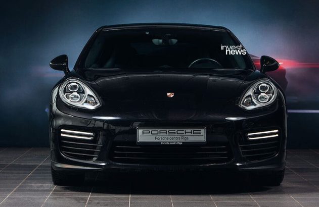 Porsche Panamera preto, vista frontal, em showroom com luzes diurnas acesas.