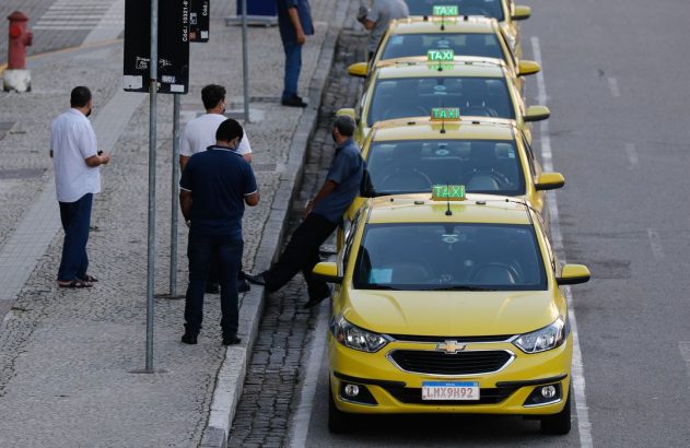 taxistas encostados nos carros em ponto de taxi