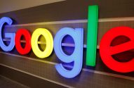 Logotipo iluminado da Google com letras 3D coloridas (azul, vermelho, amarelo, verde), fixado em uma parede de azulejos.