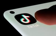 Dedo toca tela de smartphone com ícone e nome do TikTok.