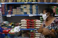 Mulher de máscara em supermercado com prateleiras cheias de arroz e aviso de limite de compra.