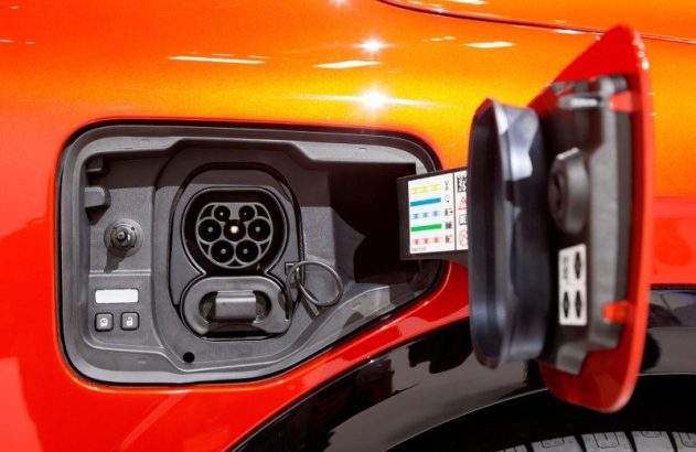 Porta de carregamento de um carro elétrico laranja aberta, mostrando o conector e informações.