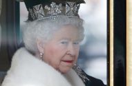 Close-up da Rainha Elizabeth II, coroa de diamantes e pérolas, casaco de pele branca, olhando à direita através de janela.