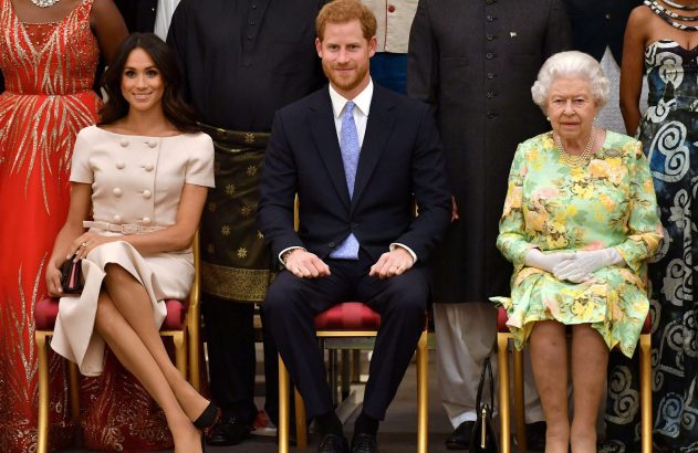 Meghan Markle, Príncipe Harry e Rainha Elizabeth II posam sentados em fila, com convidados ao fundo.