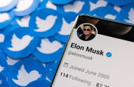 Smartphone exibe perfil de Elon Musk no Twitter, sobre múltiplos logos azuis do pássaro do Twitter.