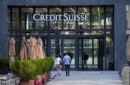 Entrada do Credit Suisse: fachada de vidro, pessoas se aproximando e guarda-sóis dobrados.