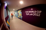 Corredor iluminado com grafismos coloridos e logo "FIFA WORLD CUP Qatar 2022" na parede. Dois homens ao fundo.