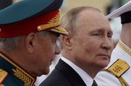 Vladimir Putin em perfil, olhando à direita, ao lado de um oficial em uniforme militar e outro militar à direita.