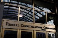 Entrada dourada da Federal Communications Commission. Letreiro e reflexos de prédio, luzes internas e número 445 na janela.