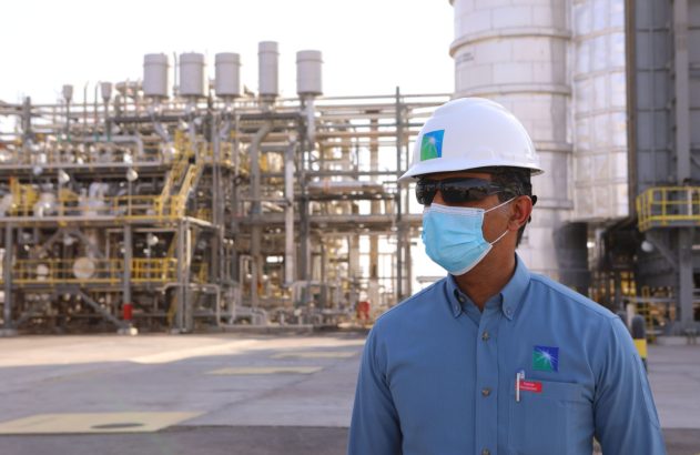 Funcionário Aramco de máscara e capacete com óculos de segurança em planta industrial.