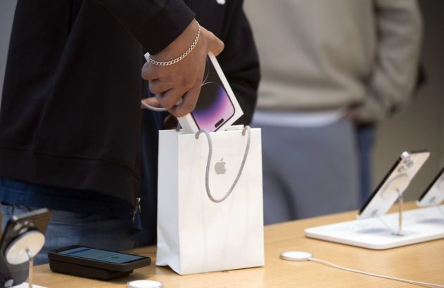 Mão colocando caixa de iPhone em sacola da Apple em loja.