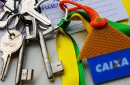 Molho de chaves com chaveiro da Caixa (casa e cartão) e fita brasileira sobre anotações.
