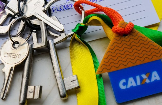Molho de chaves com chaveiro da Caixa (casa e cartão) e fita brasileira sobre anotações.