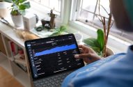 Pessoa segura tablet com app de finanças, exibindo gráfico de patrimônio e investimentos.