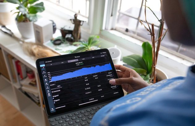 Pessoa segura tablet com app de finanças, exibindo gráfico de patrimônio e investimentos.
