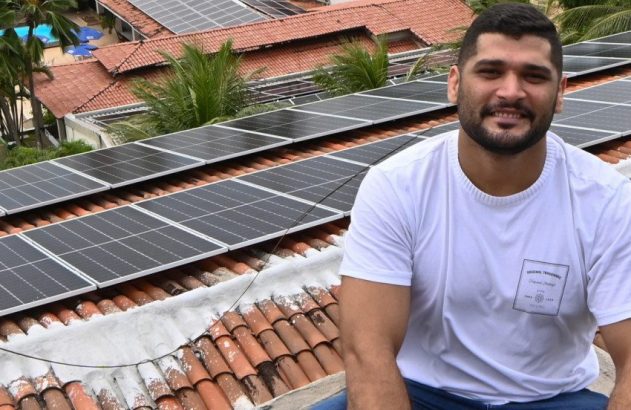Homem sorrindo em telhado com painéis solares.