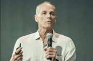 Palestrante, segurando microfone e controle, fala durante apresentação.