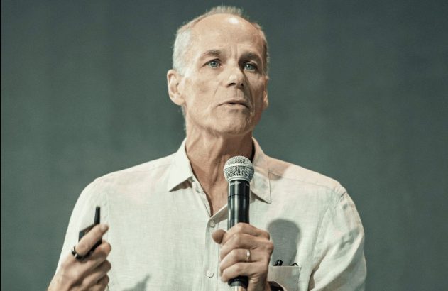 Palestrante, segurando microfone e controle, fala durante apresentação.