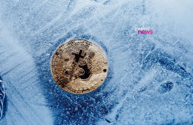 Bitcoin dourado e reluzente incrustado em um bloco de gelo translúcido com muitas bolhas.