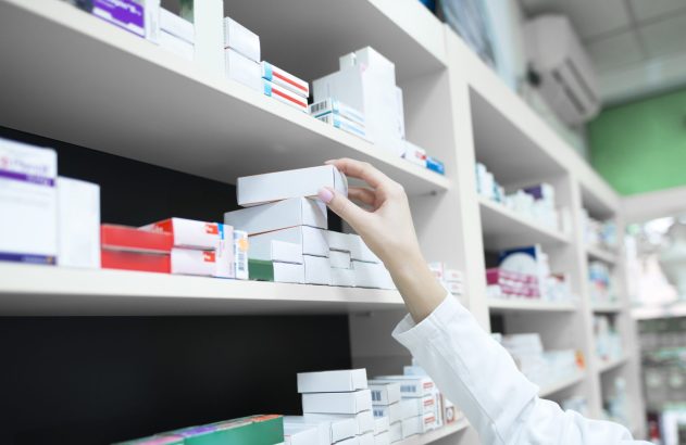 Mão colocando caixa branca em prateleira de farmácia.