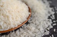 Arroz branco em tigela de madeira e espalhado em superfície escura.