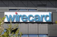 Logotipo azul "Wirecard" com um ponto vermelho em um edifício com persianas e vegetação.