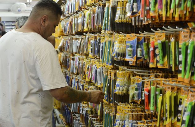 Homem seleciona produtos de papelaria BIC (canetas, lápis) em expositor de loja.