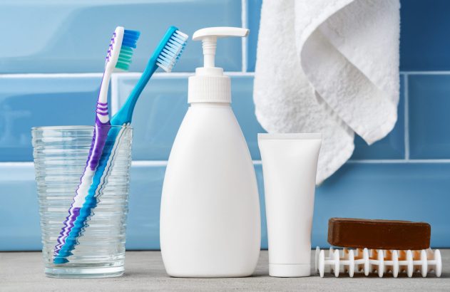 Itens de higiene pessoal no banheiro: escovas de dente em copo, sabonete líquido, pasta de dente, sabonete em barra e toalha.