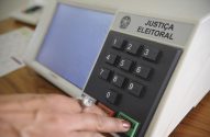 Mão de eleitor(a) confirmando voto em urna eletrônica da Justiça Eleitoral.