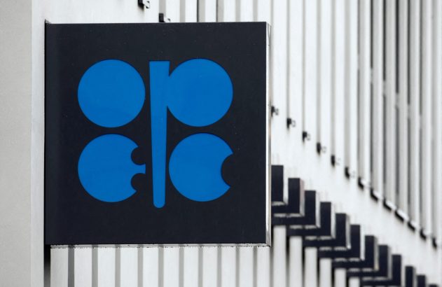 Sinal da OPEC em preto e azul, fixado em uma estrutura com barras verticais claras.