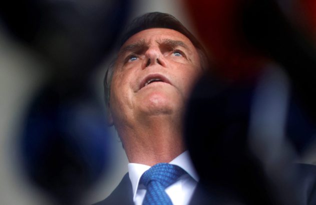 Jair Bolsonaro, de terno e gravata, olhando para cima em um fundo desfocado.