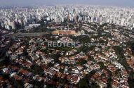 Cenário urbano: estádio de futebol cercado por casas e edifícios altos ao fundo.