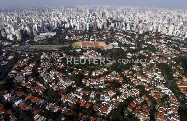 Cenário urbano: estádio de futebol cercado por casas e edifícios altos ao fundo.