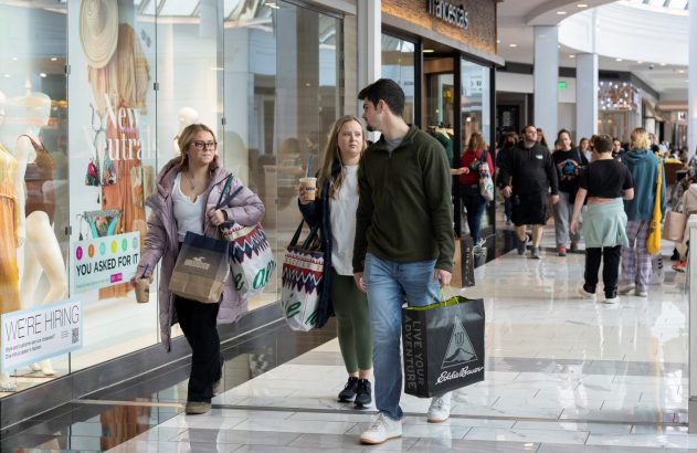 Grupo de pessoas com sacolas de compras caminhando por um shopping.