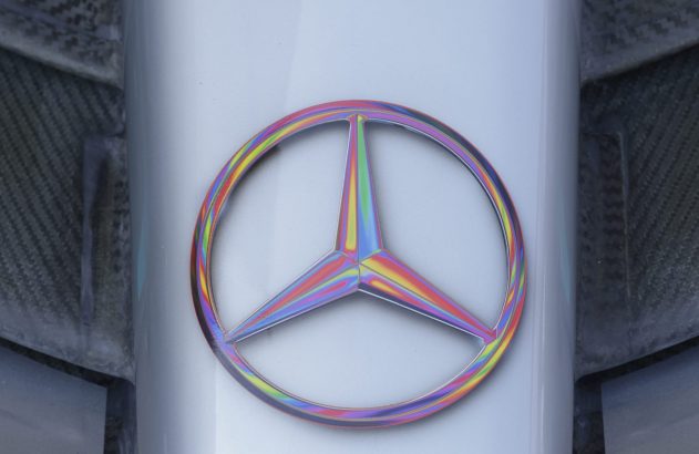 Logo Mercedes-Benz iridescente em fundo cinza, com fibra de carbono nas laterais.