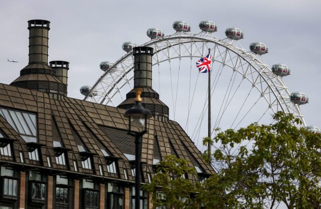 London Eye, bandeira britânica e prédio com chaminés sob céu cinzento. Avião e folhagem.