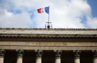 Bandeira francesa voa sobre fachada de prédio com "BOURSE" em letras douradas e colunas. Céu nublado.
