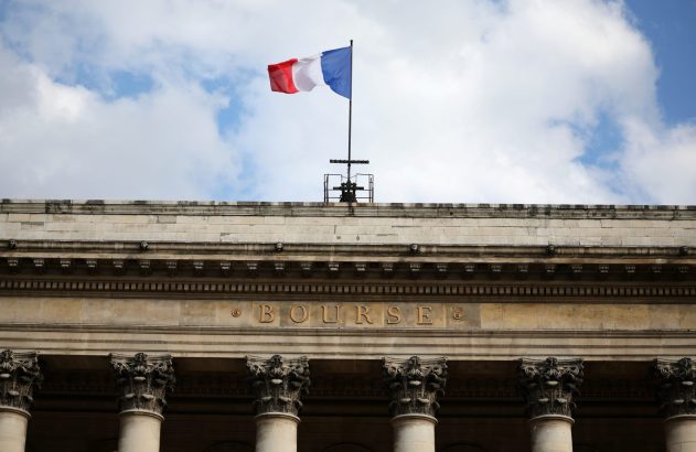 Bandeira francesa voa sobre fachada de prédio com "BOURSE" em letras douradas e colunas. Céu nublado.