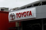 Letreiro Toyota vermelho e branco em um prédio, com showroom e carros visíveis.