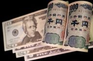 Cédulas de dólar e duas cédulas de 1000 ienes japoneses enroladas, sobre fundo escuro.