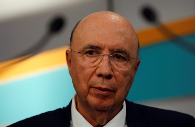 Close-up de homem careca com óculos e terno. Ele olha à frente contra fundo abstrato azul e amarelo.