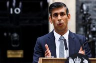 Rishi Sunak, de terno e gravata, discursa em pódio com brasão real, em frente à porta 10 de Downing Street.