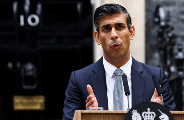 Rishi Sunak, de terno e gravata, discursa em pódio com brasão real, em frente à porta 10 de Downing Street.