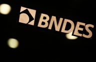 Logo e nome BNDES em letras metálicas douradas e brilhantes, sobre fundo escuro com pontos de luz.