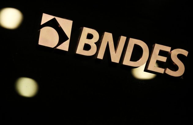 Logo e nome BNDES em letras metálicas douradas e brilhantes, sobre fundo escuro com pontos de luz.