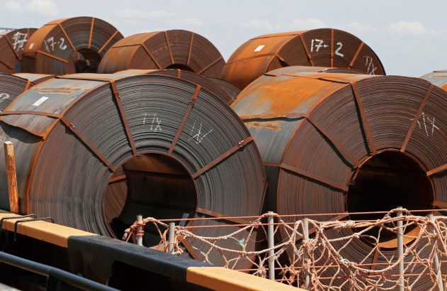 Grandes bobinas de aço enferrujadas com marcações brancas, a bordo de um navio.