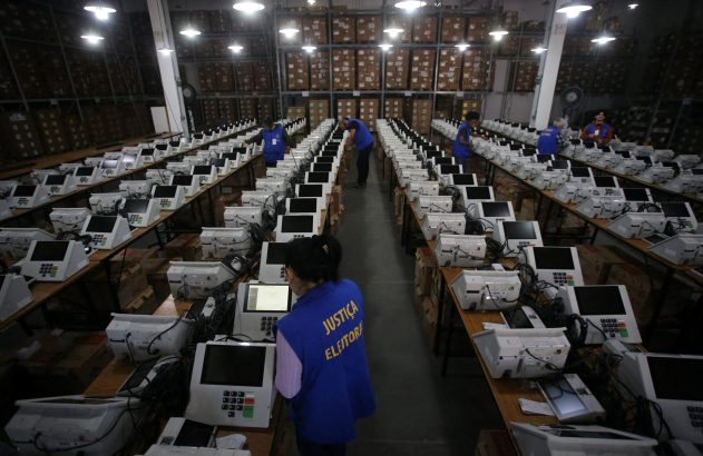 Em armazém, equipe da Justiça Eleitoral configura fileiras de urnas eletrônicas para as eleições.